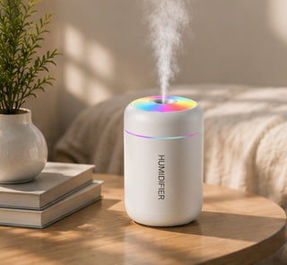 Difusor blanco encendido en una mesita junto a una planta y unos libros