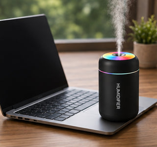 Difusor negro funcionando en un escritorio al lado de un portatil