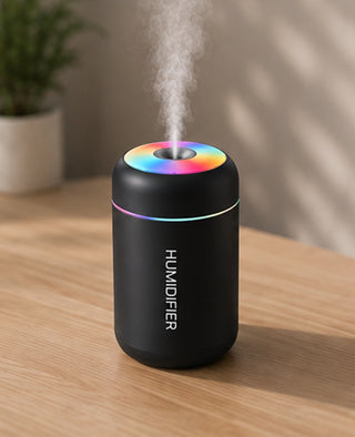Difusor negro encendido sobre una mesa de madera con una planta detras