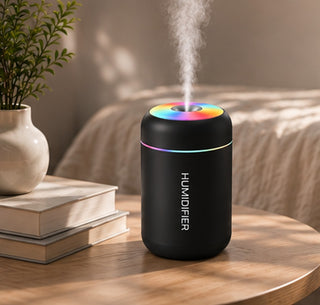 Difusor negro encendido en una mesita junto a una planta y unos libros