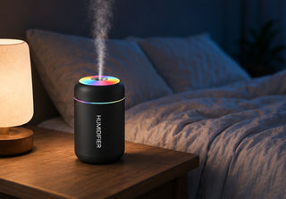 Difusor negro encendido en la mesilla de noche junto a una lampara